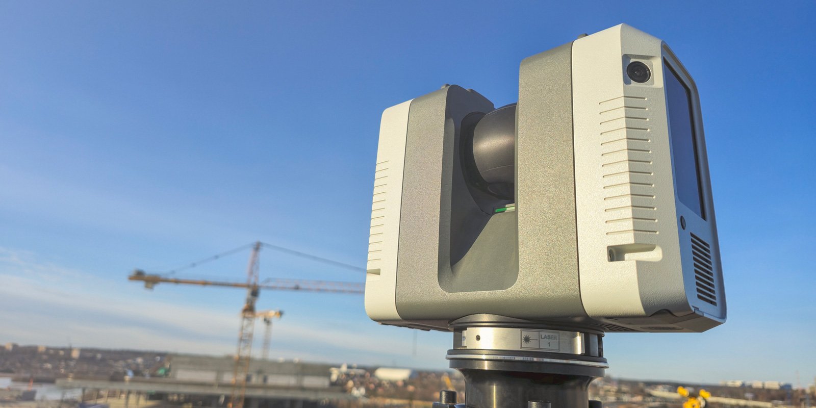 High-tech 3D laser scanner on a tripod at a construction site with a crane in the background under a clear blue sky.