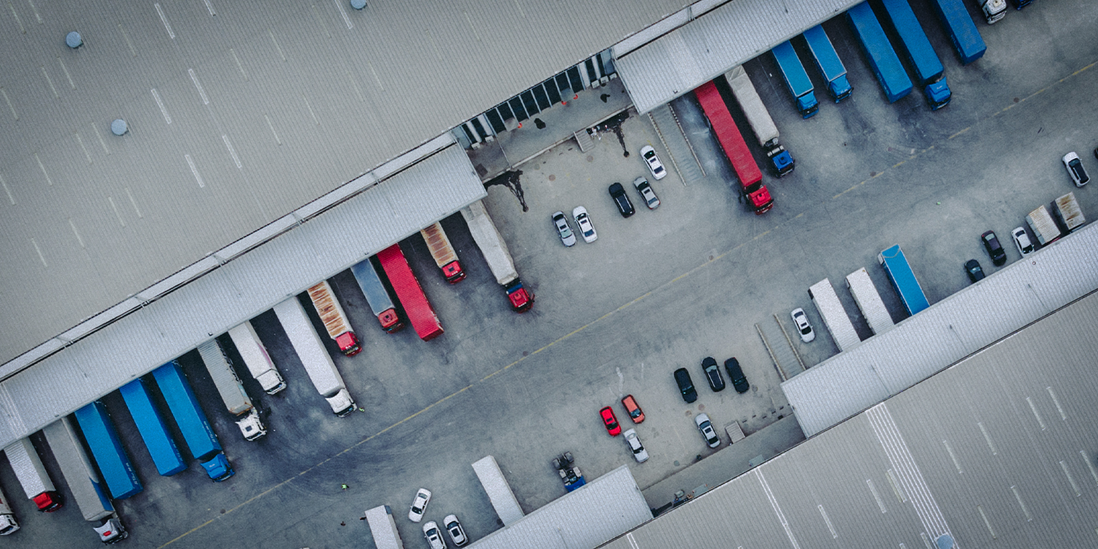 Aerial view of a logistics distribution center with multiple semi-trucks backed into loading docks, showing organized freight operations and parked vehicles.
