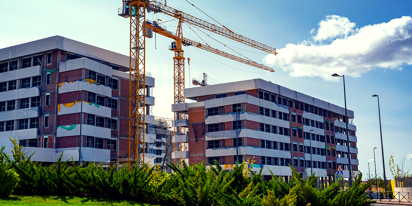 Construction cranes over partially built mid-rise residential buildings under a blue sky.