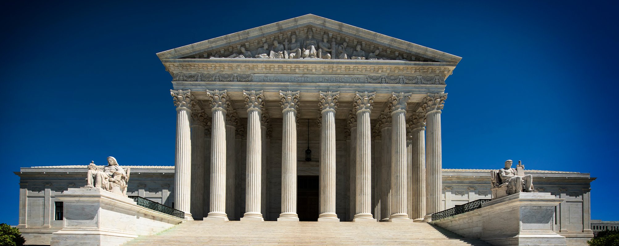 Front view of the United States Supreme Court building in Washington D.C., showcasing classical architecture with tall columns and blue sky background.