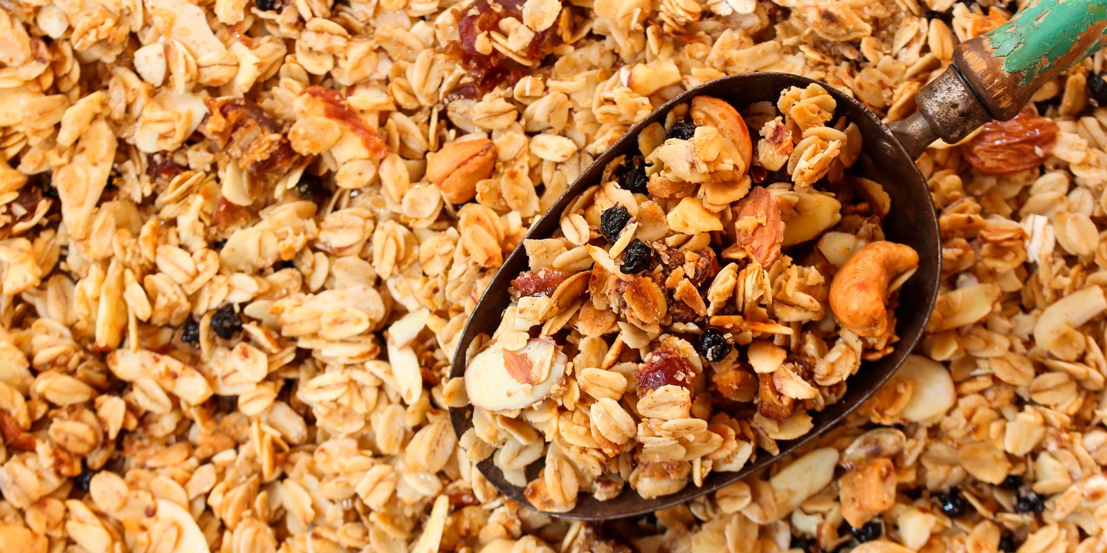 Scoop of homemade granola with oats, nuts, seeds, and dried fruit.