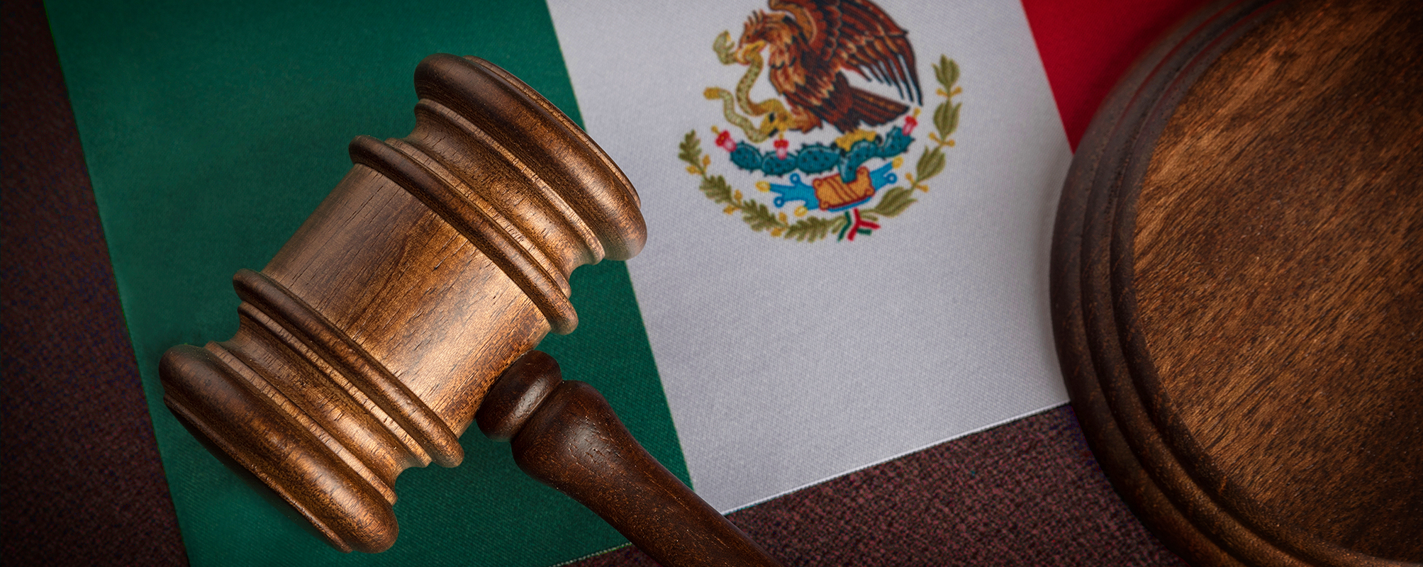 Wooden gavel and sound block on top of the Mexican flag, symbolizing law and justice in Mexico.