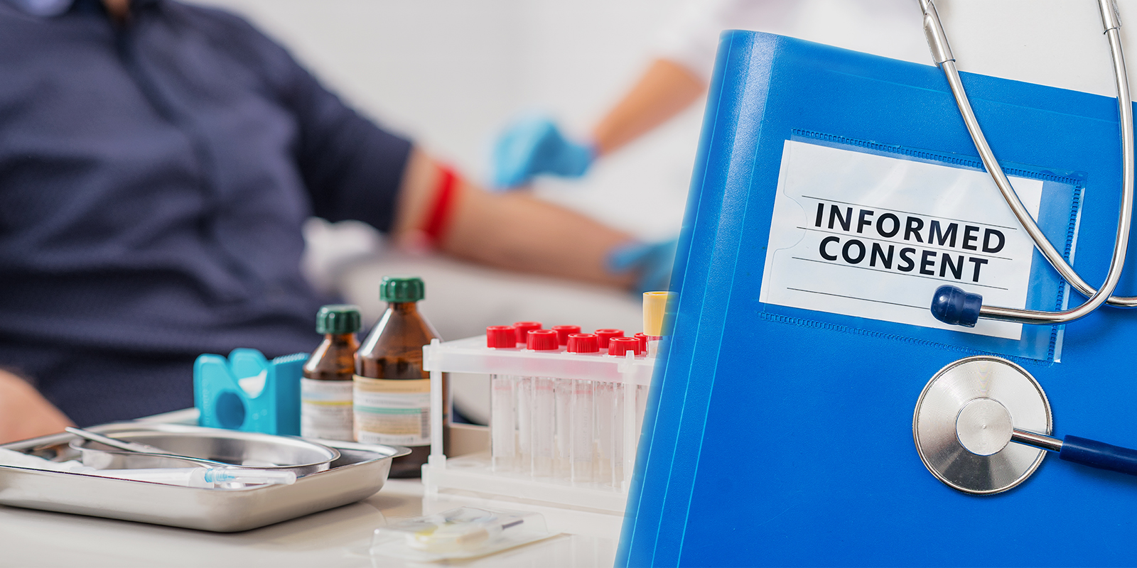Close-up of a blue folder labeled 'Informed Consent' with medical equipment and a patient receiving a blood draw in the background.